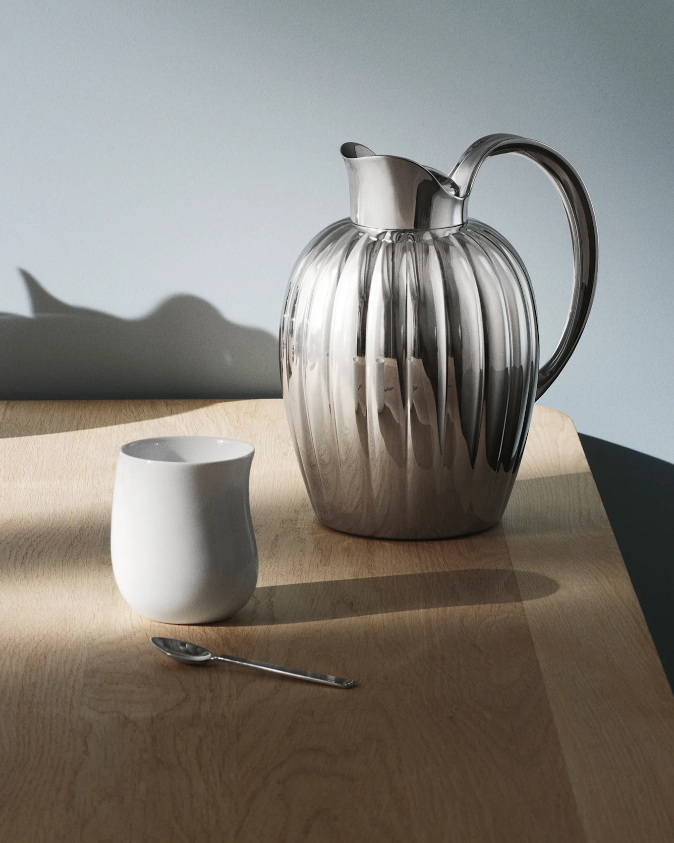 Μια λαμπερή, ραβδωτή ασημένια κανάτα με χερούλι σε ένα σκούρο, ανακλαστικό τραπέζι, με σχέδια φωτός.