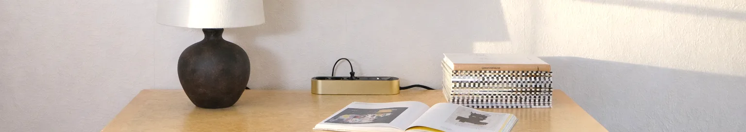 Χρυσή πολύπριζο με τρεις μαύρες πρίζες και κουμπί λειτουργίας σε ανοιχτόχρωμη επιφάνεια.