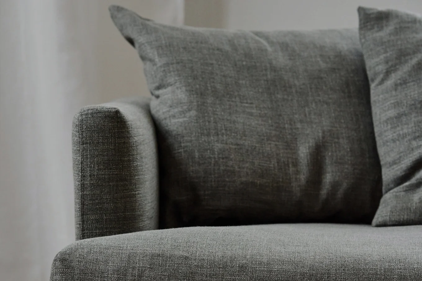 Κοντινό πλάνο ενός γκρι υφασμάτινου καναπέ με ανάγλυφα μαξιλάρια, που δείχνει το υποβραχιόνιο και το κάθισμα.