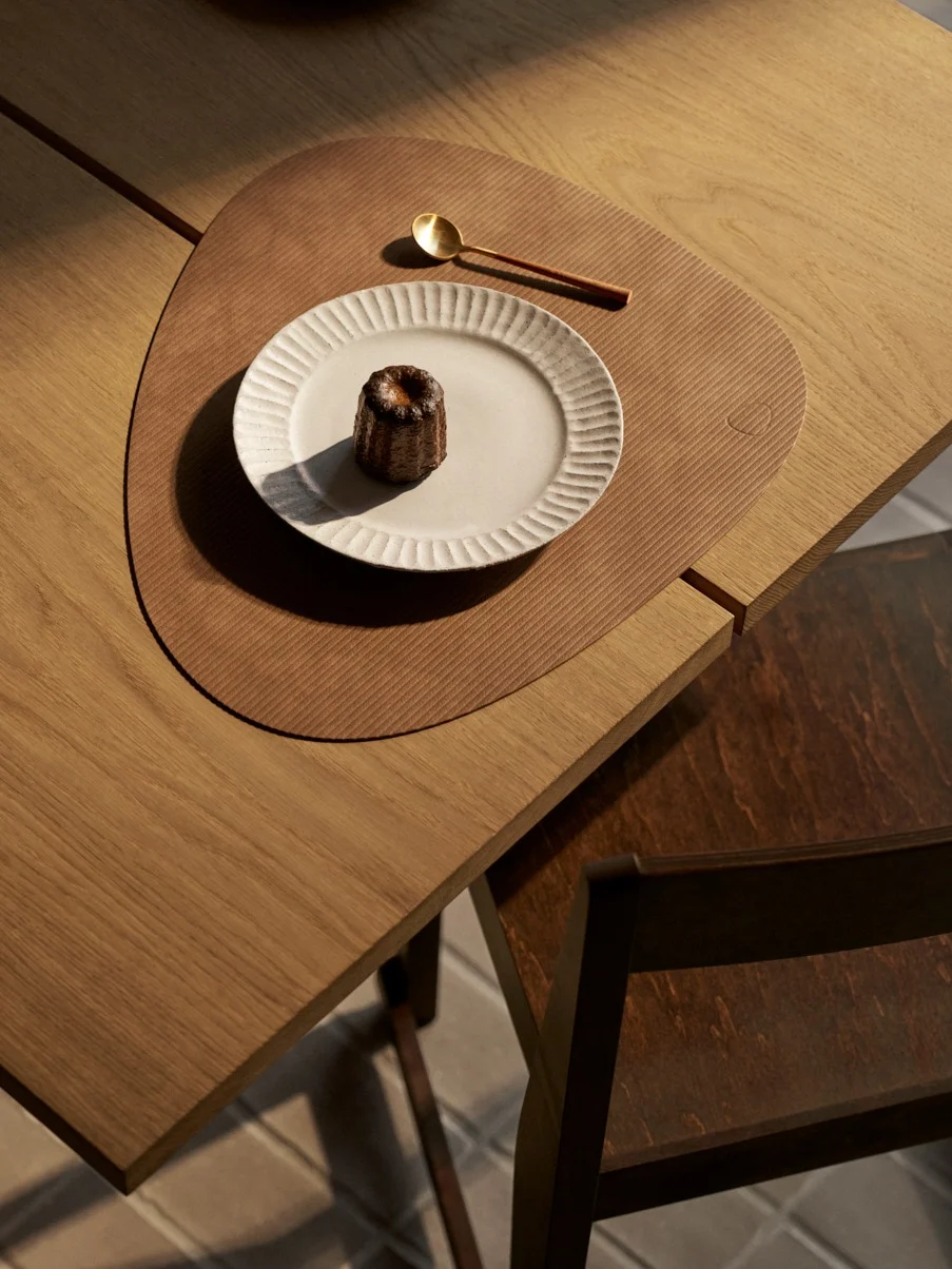 Από πάνω: κανελέ σε λευκό πιάτο, χρυσό κουτάλι σε καφέ σουπλά, ξύλινο τραπέζι.