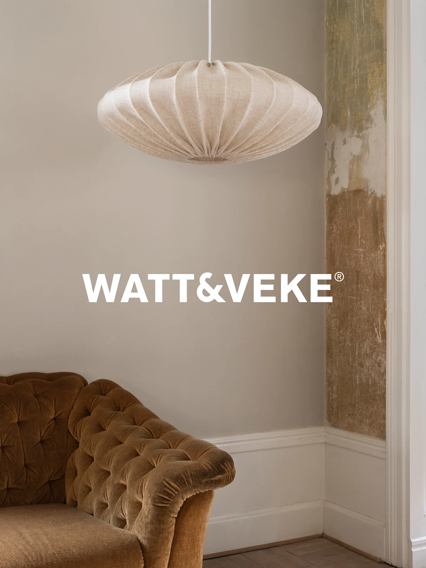 Μπεζ πτυχωτή υφασμάτινη λάμπα πάνω από καφέ βελούδινο καναπέ σε δωμάτιο με φθαρμένο τοίχο.