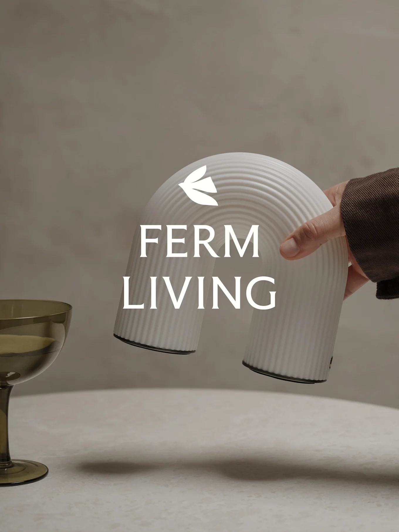 Χέρι κρατά ένα λευκό ραβδωτό διακοσμητικό αντικείμενο σε σχήμα τόξου, με ένα πράσινο ποτήρι κοντά.