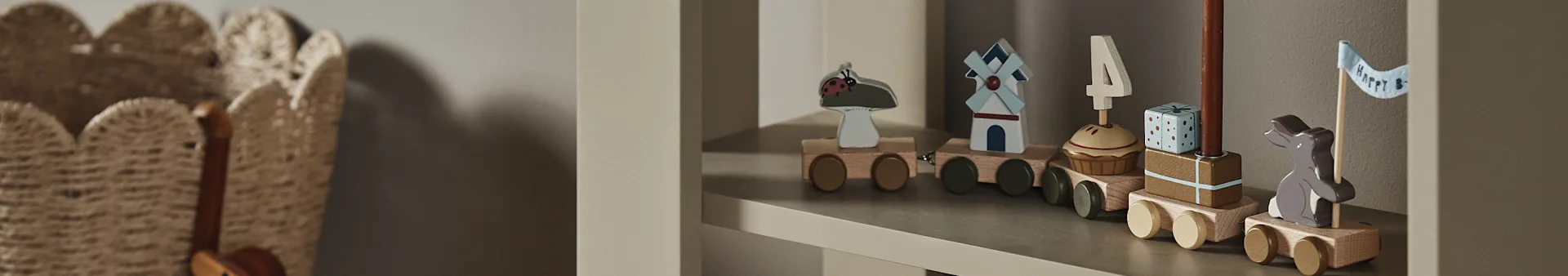 Ένα ξύλινο τρενάκι σε ράφι, με βαγόνια που απεικονίζουν μια πασχαλίτσα, ανεμόμυλο, cupcake με κερί '4', δώρο και λαγουδάκι με σημαία "Happy B".