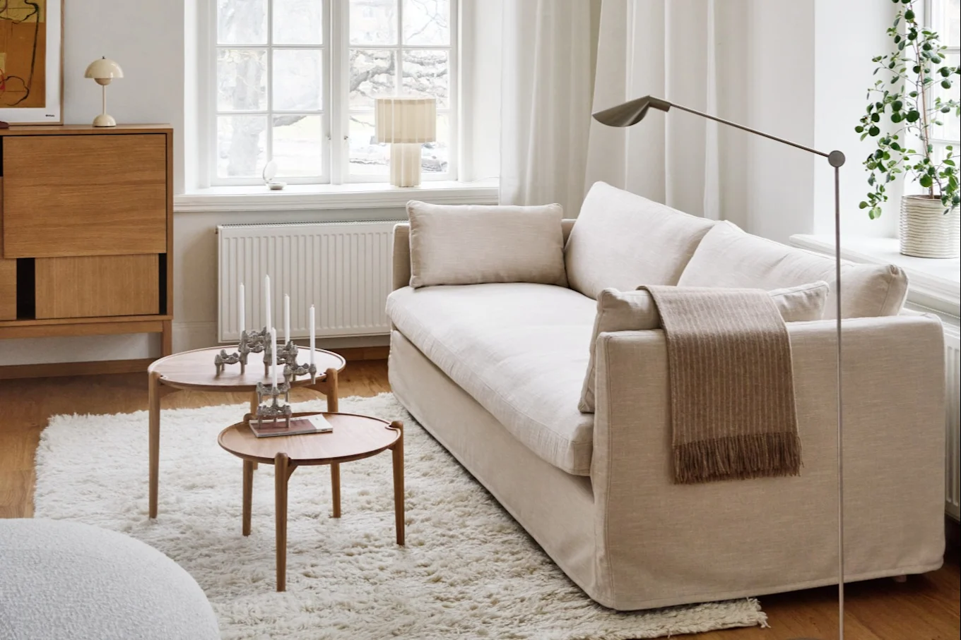 Ένα άνετο σαλόνι με ανοιχτόχρωμο καναπέ, δύο στρογγυλά ξύλινα τραπεζάκια σαλονιού, ένα χνουδωτό χαλί και ένα ξύλινο ντουλάπι.