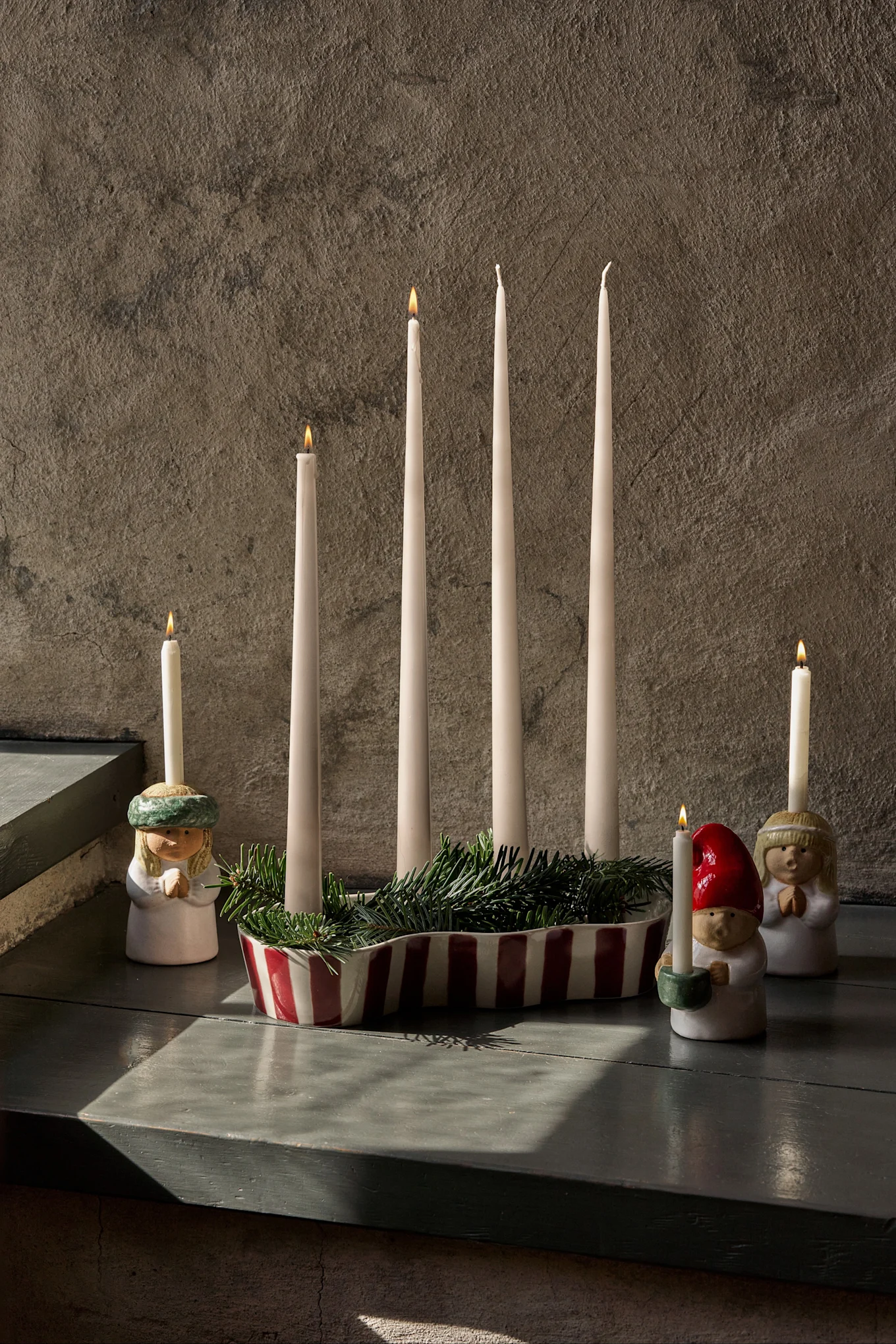 Διακόσμηση Advent με τέσσερα άκαυστα κεριά, κλαδιά έλατου και τρεις φιγούρες με αναμμένα κεριά.