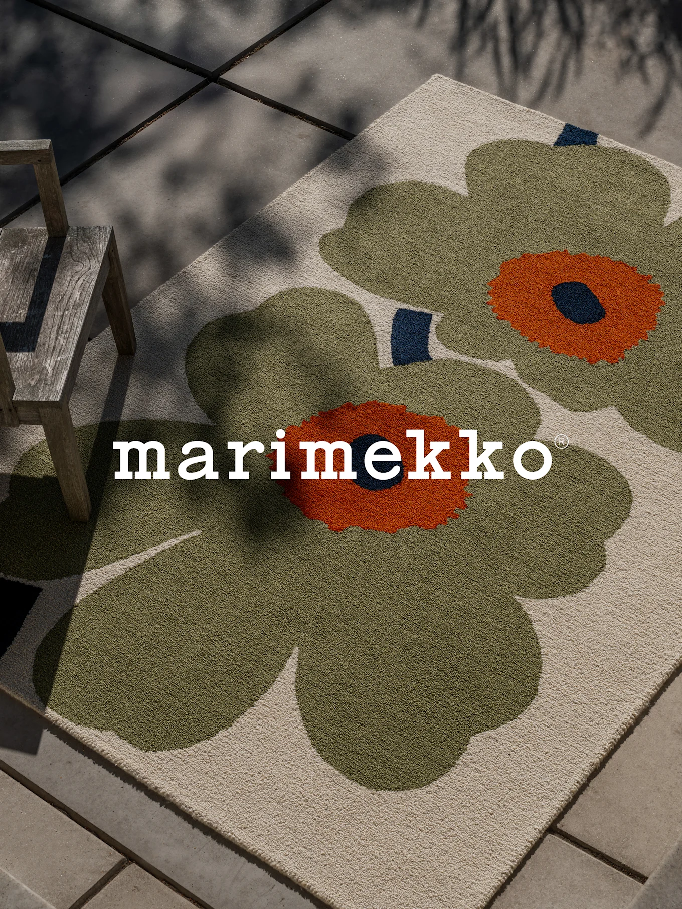 Χαλί Marimekko με μεγάλο πράσινο και πορτοκαλί floral σχέδιο σε βεράντα με ξύλινη καρέκλα.